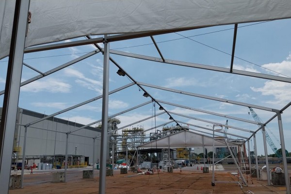 view from inside partially built tent frame roof structure looking out at industrial plant with crane, exposed aluminium trusses