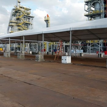 white sloped tent roof structure next to large petrochemical plant facility, worker in orange coveralls, industrial pipes and towers